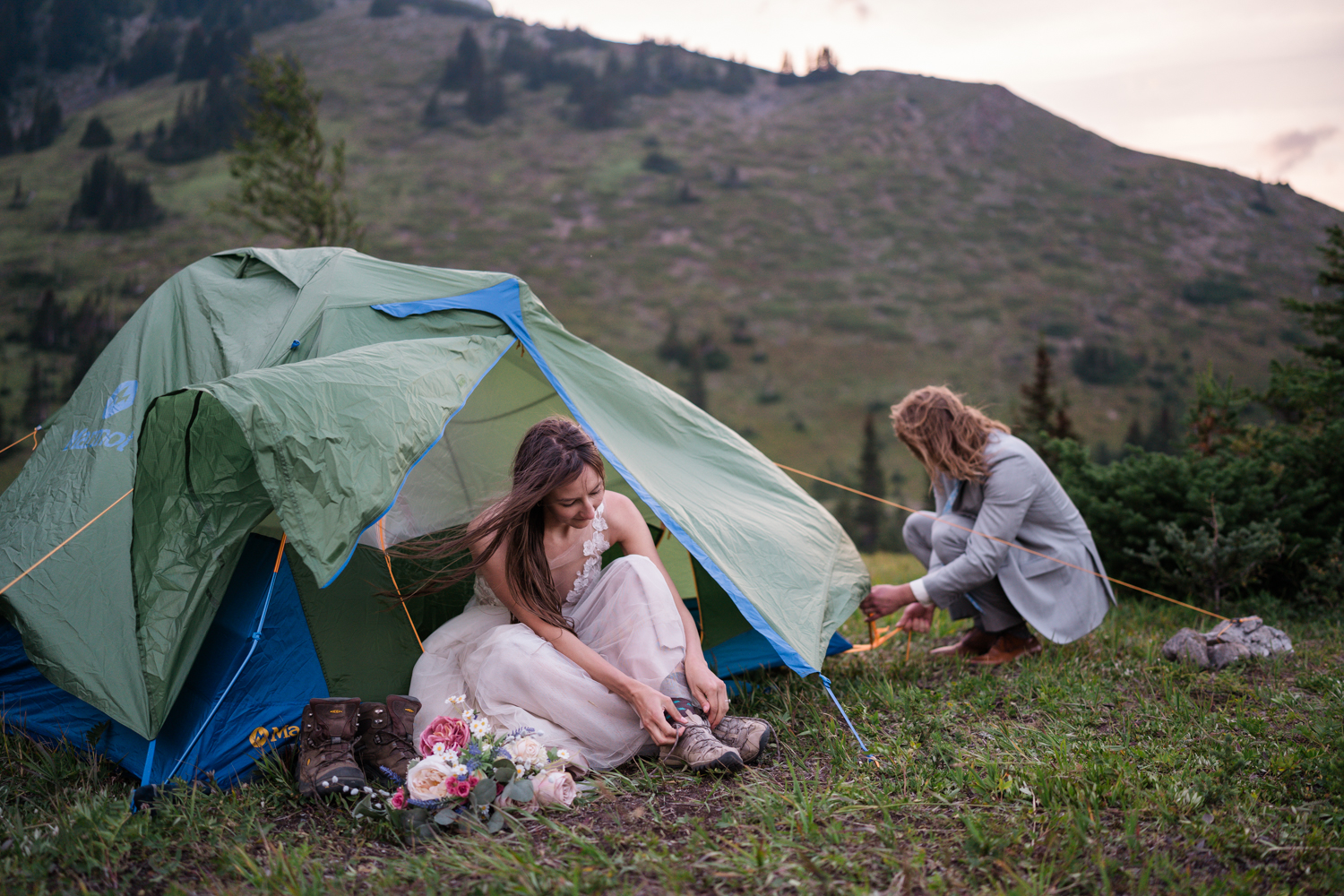 bride in wedding dress sits in vestibule of tent tying up her hiking boots 