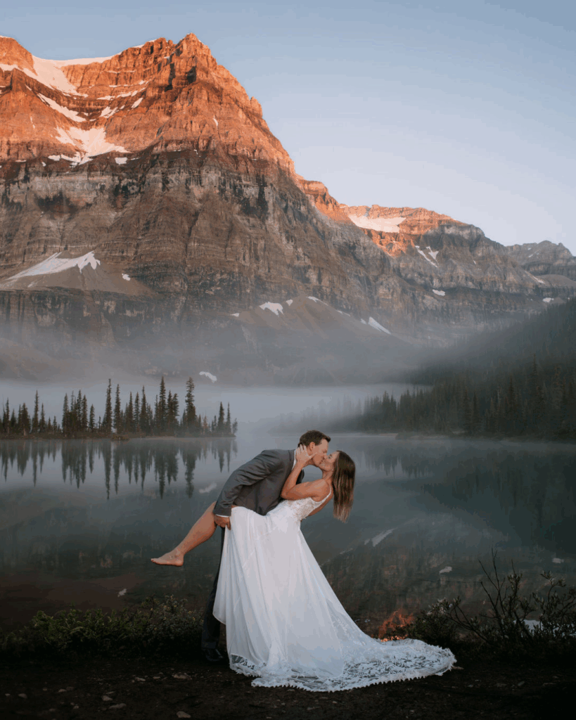 Groom dips barefoot bride in front of a misty lake and alpenglow during Shadow Lake Lodge elopement