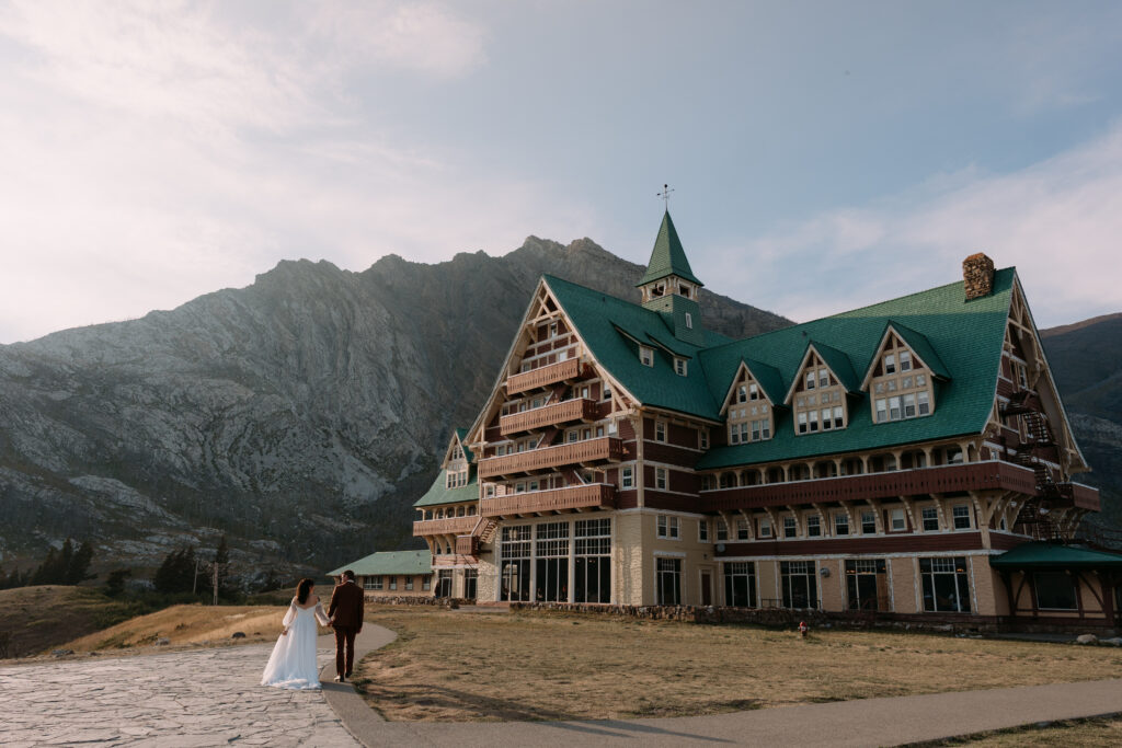 couple in wedding attire walks towards Prince of Wales Hotel after Waterton elopement