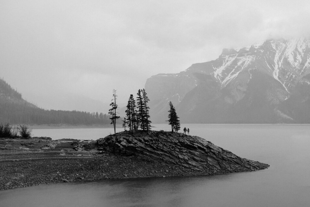 couple stands on rock in lake minnewanka in the rain