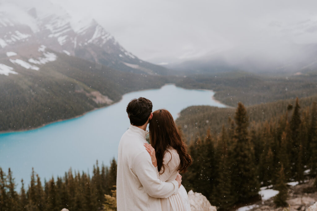 snow falls as couple looks out at peyto lake during banff engagement