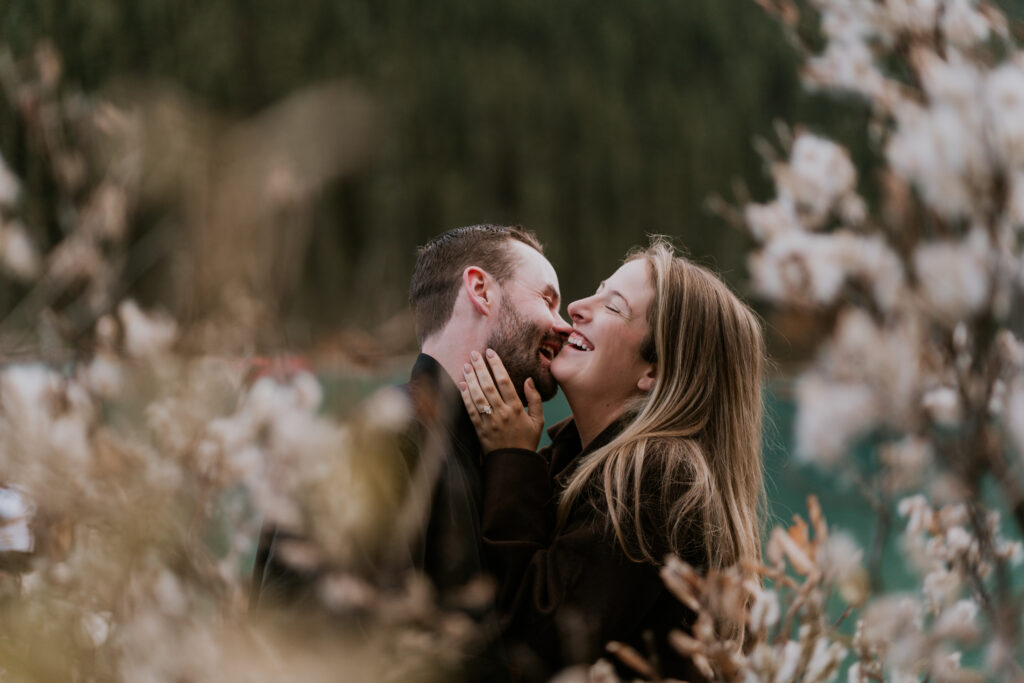 couple laughs together in front of fireweed that has gone to seed after lake louise proposal
