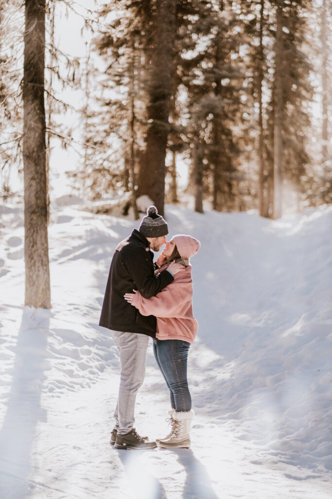 couple kisses in trees at lake minnewanka during winter proposal