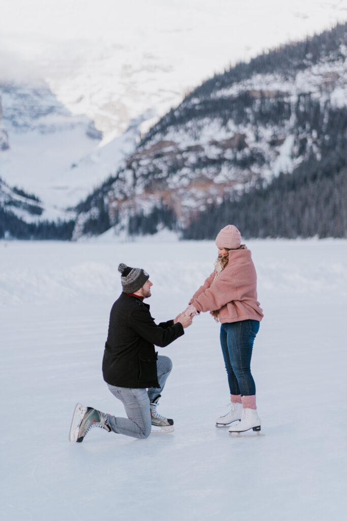 man is down on one knee wearing skates while proposing to his girlfriend on a frozen lake louise