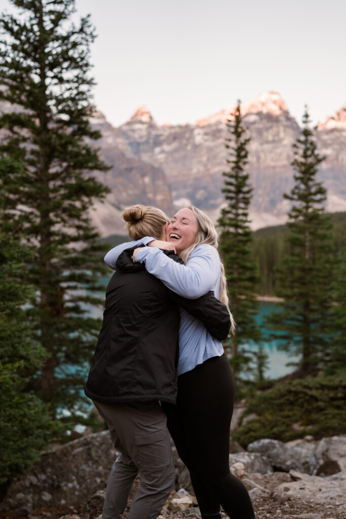 two girls hug as the sun comes up at moraine lake after they got engaged