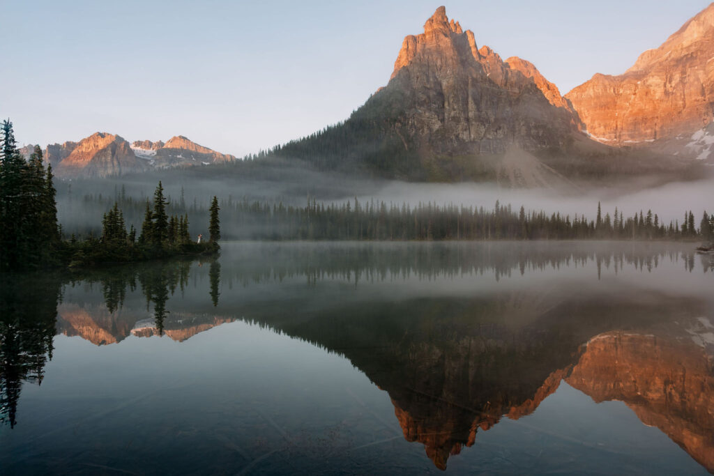 Couple stands on shoreline during sunrise at Shadow Lake Lodge 