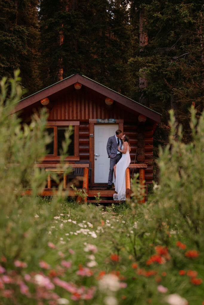 couple kisses on porch of Shadow lake lodge cabin in front of wildflowers during elopement