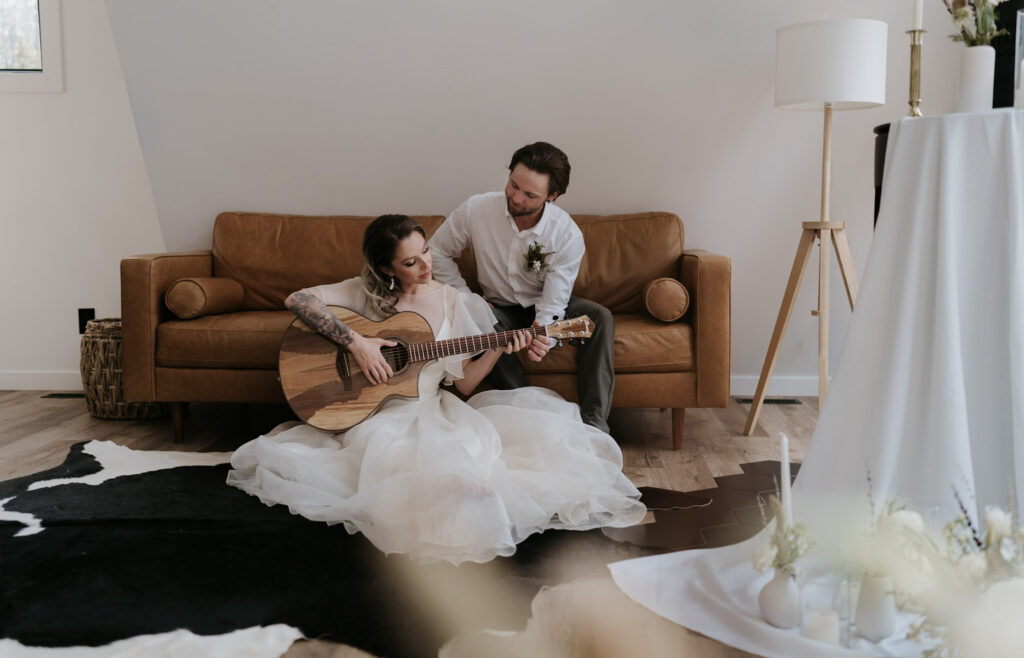 bride sits in front of couch playing guitar at Beaver Lodge A Frame cabin