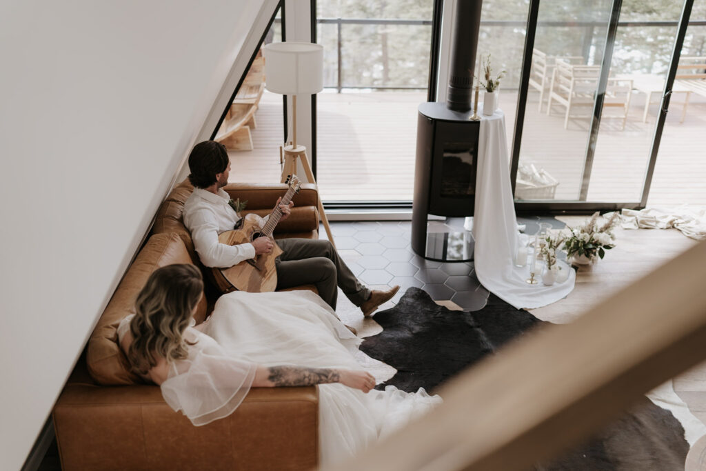groom plays guitar on couch with bride during nordegg cabin elopement
