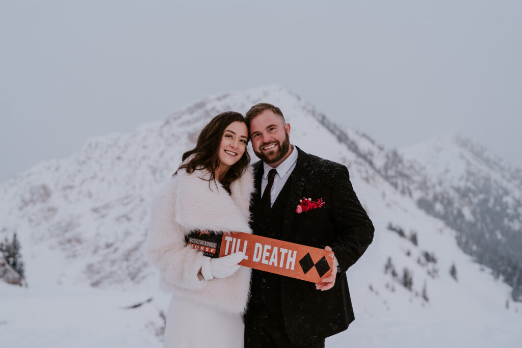 bride and groom hold custom sign during winter kicking horse mountain elopement