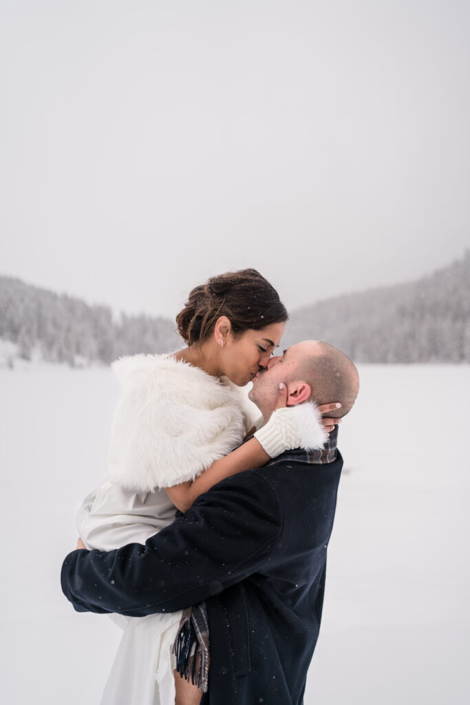 groom holds bride up while kissing her during snowy banff elopement showing off her white bridal gloves