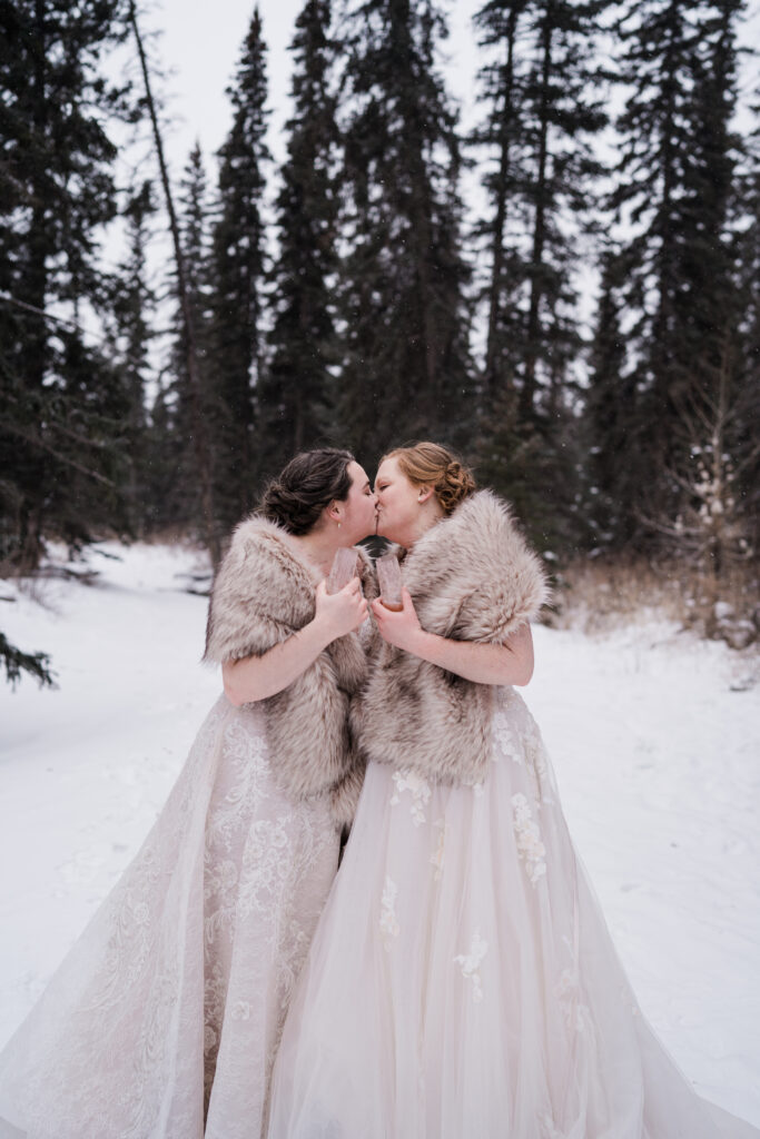 two brides kiss during winter wedding while both wear fur shawls 