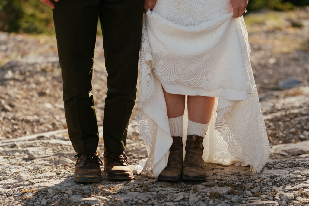 bride and groom stand side by side holding up dress to show off elopement boots 