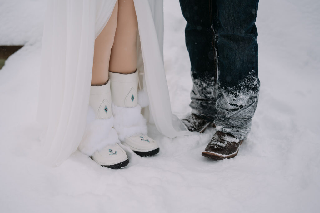 bride and grooms feet during winter banff elopement, bride wearing white mukluks and groom wearing cowboy boots. 