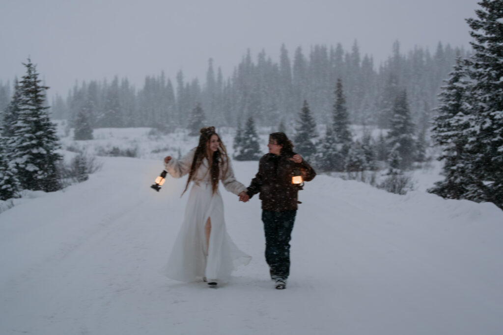 bride and groom holding lanterns run towards the camera during snowy banff elopement