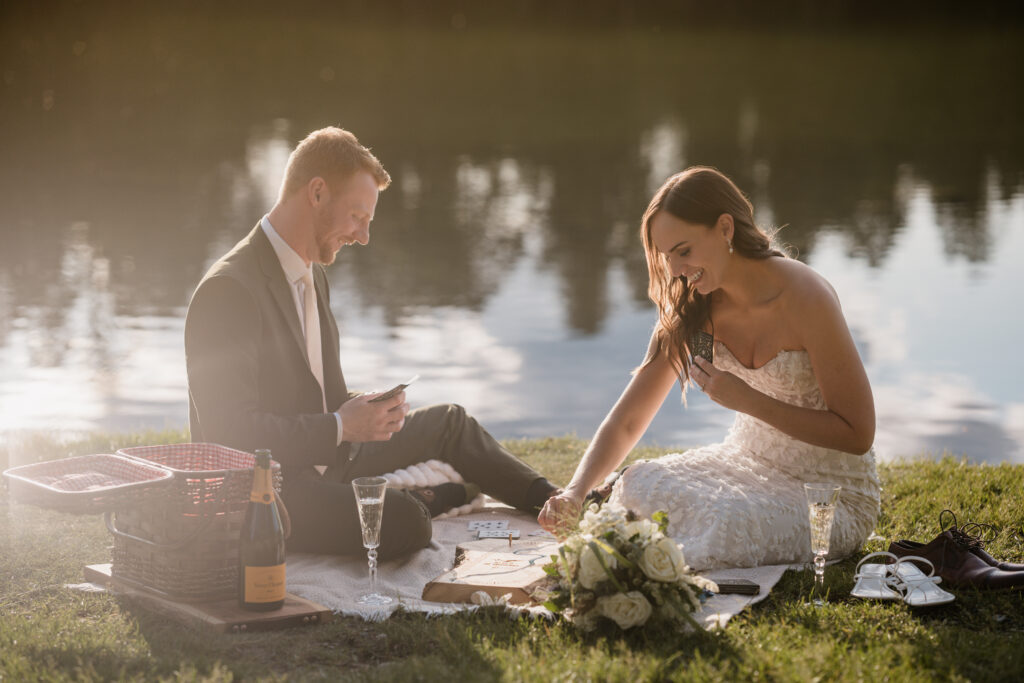 couple plays crib on blanket lakeside during sunset elopement 