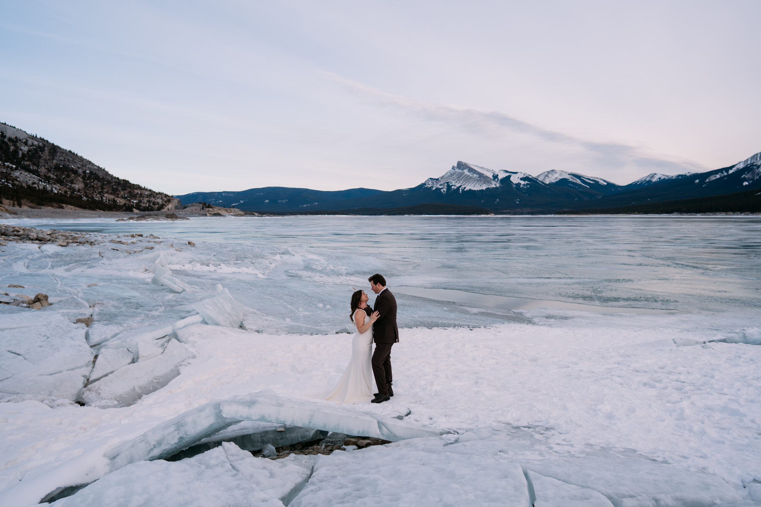 bride and groom stand looking at each other on ice chunks during winter Abraham Lake elopement