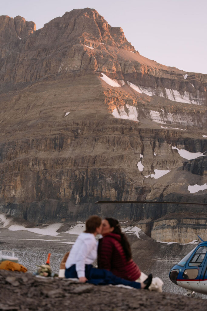 brides kiss while having a picnic during sunset helicopter elopement in Banff