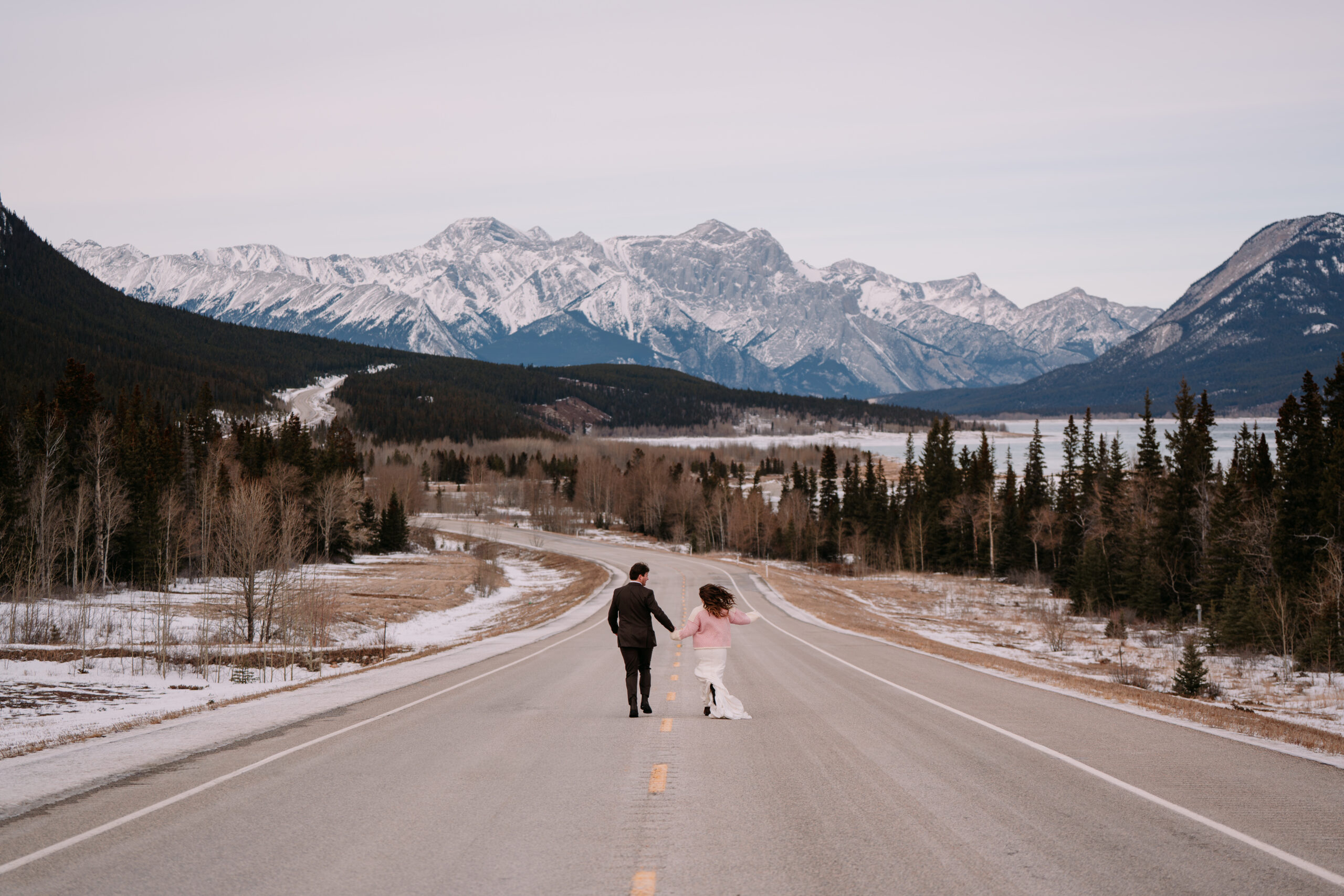 Bride and groom run down road during winter elopement in Nordegg