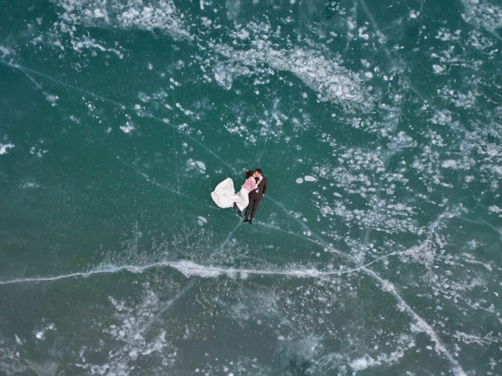 drone photo of bride and groom laying on ice with methane bubbles around them during winter Abraham Lake Elopement