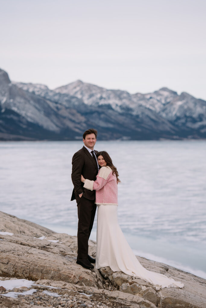 bride in knit pink sweater cuddles into groom during winter elopement in Canada