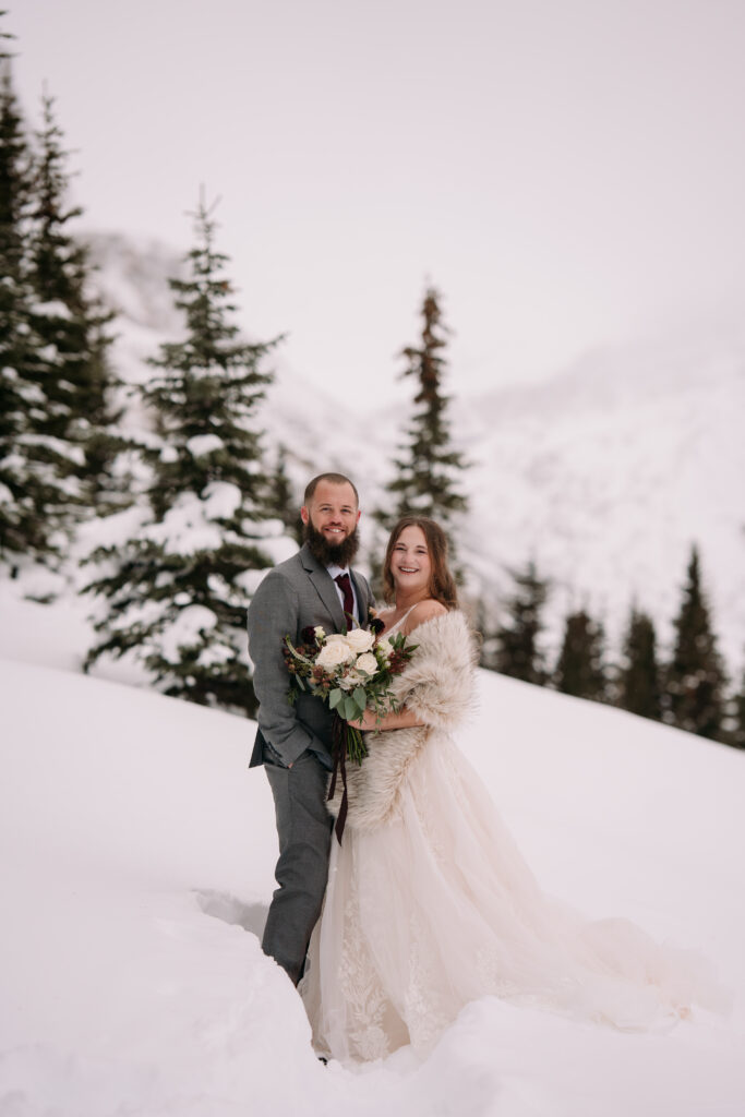 bride and groom look towards camera laughing during winter elopement. shes's wearing a fur shawl. 