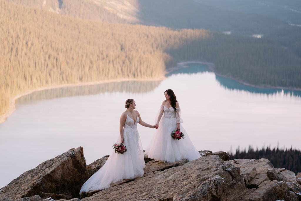 two brides with flowers stand on rock overlooking peyto lake