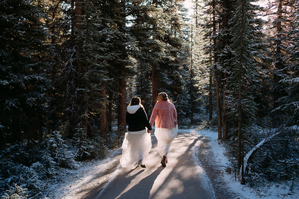 two brides walk down pathway in snow in banff national park 