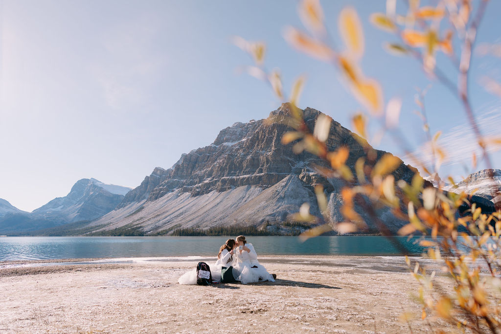 brides sit on blanket at bow lake during october elopement