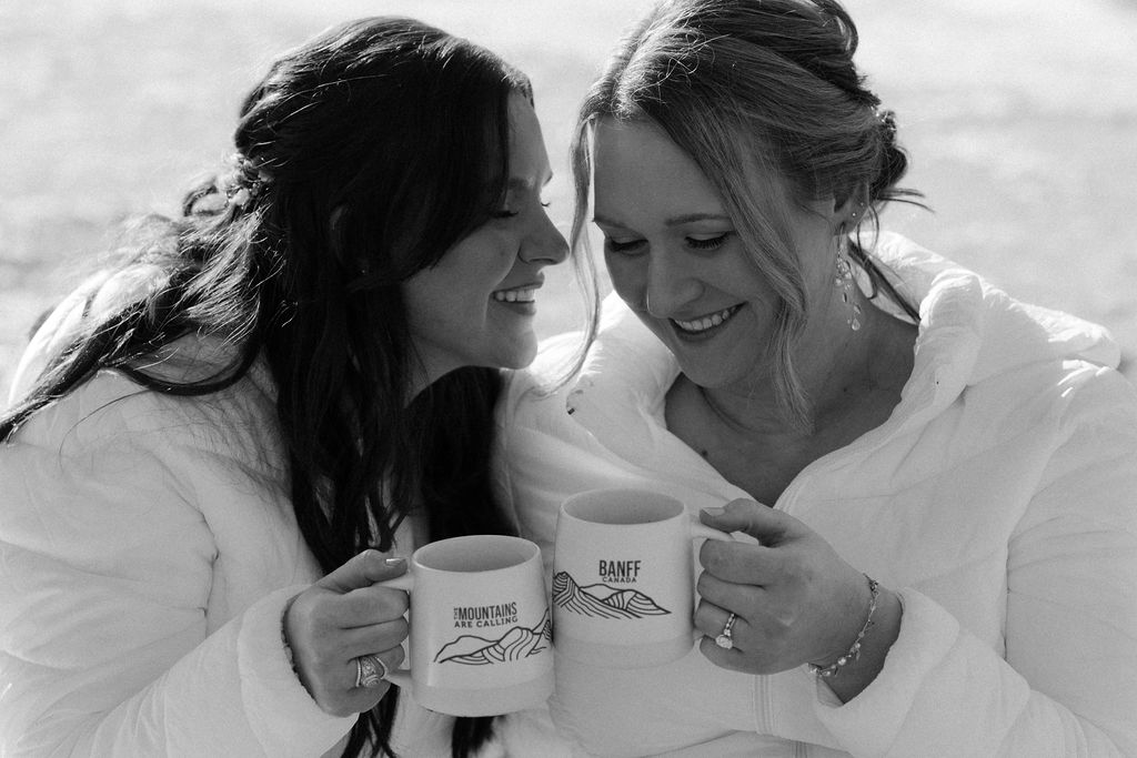 brides laugh with each other holding banff mugs during elopement