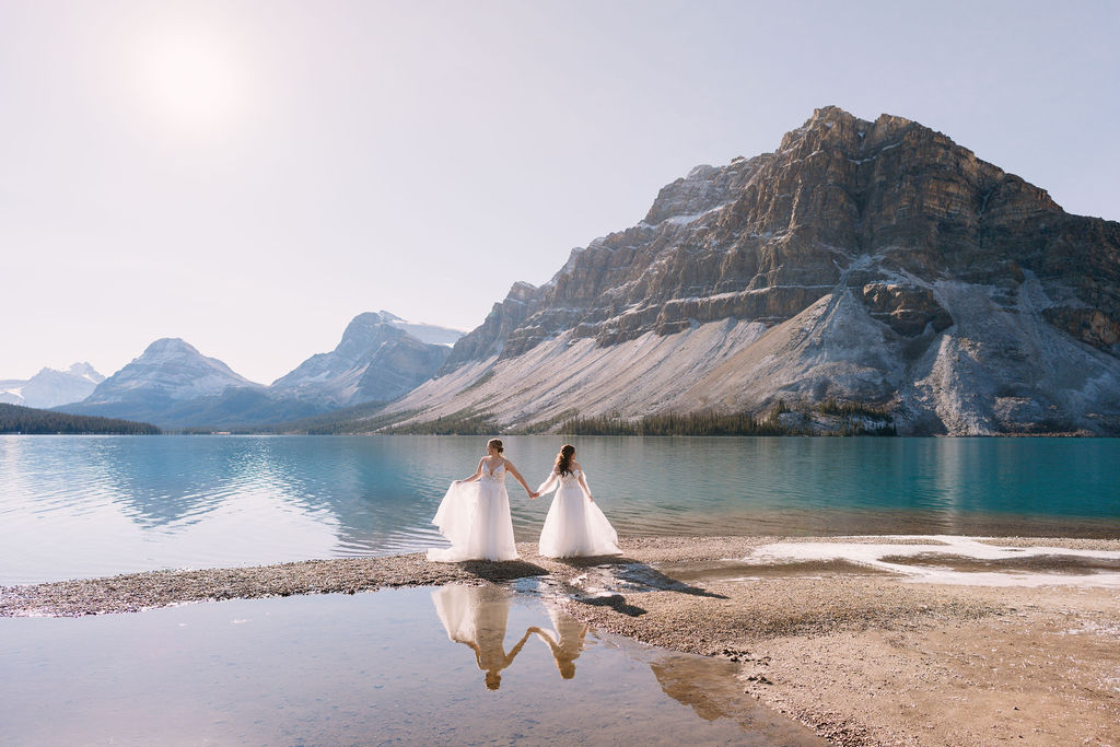 sun shines through brides wedding dresses on the shoreline of Bow Lake during elopement