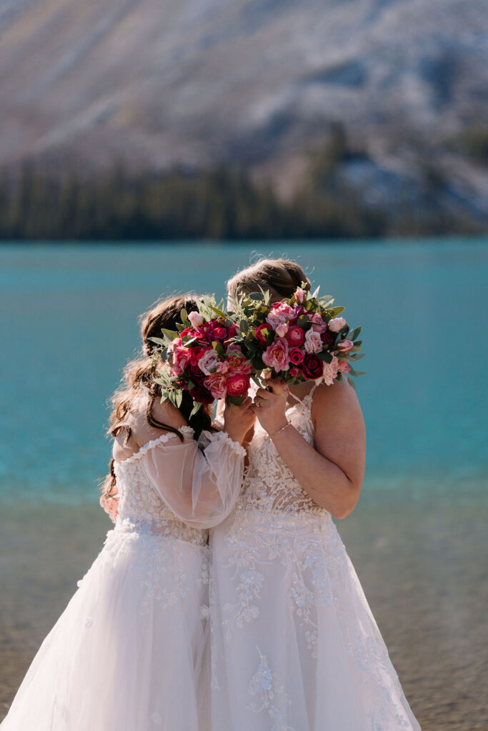 Brides hold bouquets in front of their faces while kissing