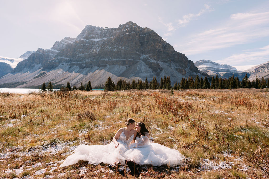 Brides snuggle up in field during October Bow Lake elopement