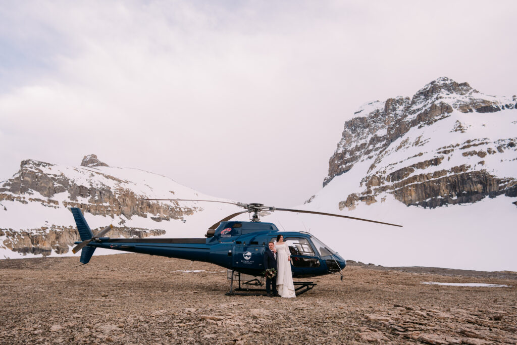 couple poses with helicopter during May elopement in the Canadian Rockies