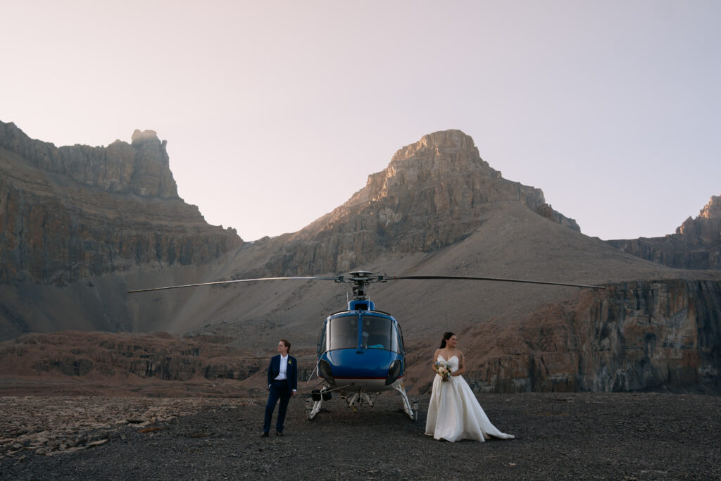 couple stands on each side of a blue helicopter looking opposite directions during Canadian Rockies helicopter elopement