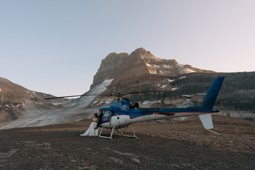 couple poses beside helicopter in the mountains at sunset during elopement