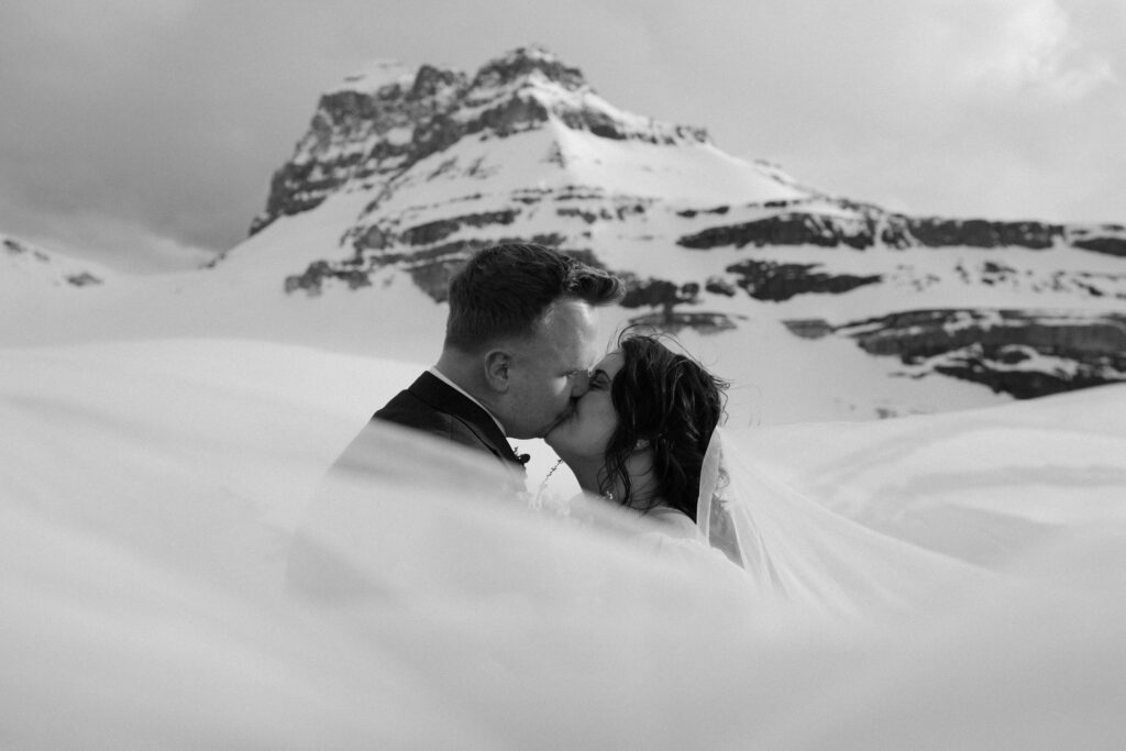 black and white of couple kissing with wind blowing the veil infront of them
