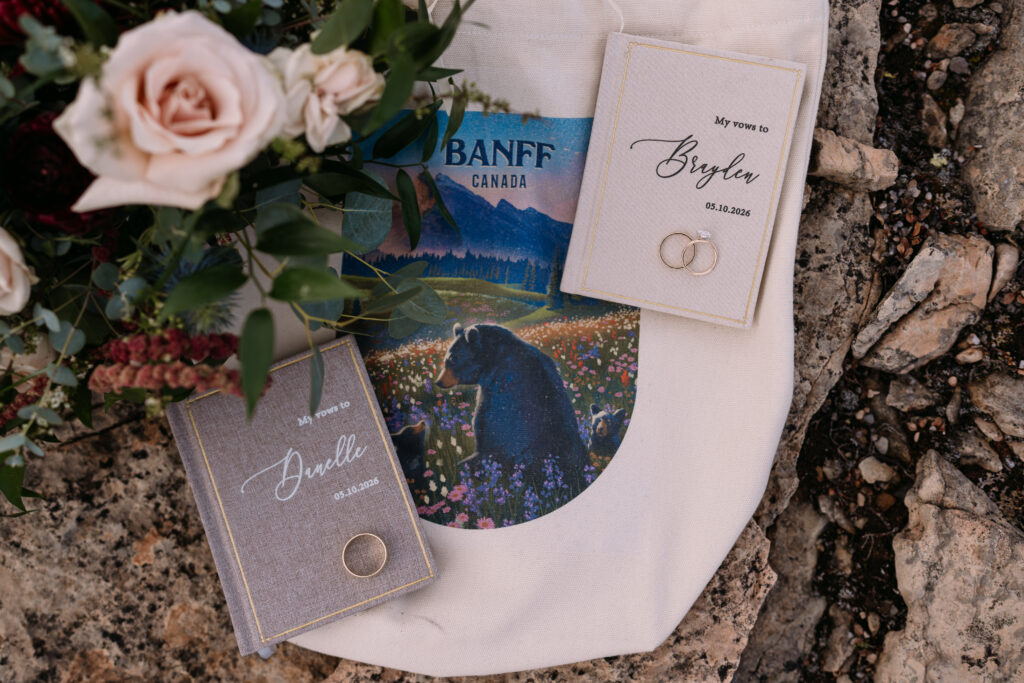 flatlay with flowers, banff canada bag, vow books, and rings during helicopter elopement