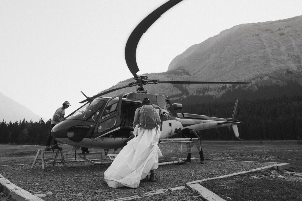 black and white of bride in wedding dress climbing into a helicopter before elopement