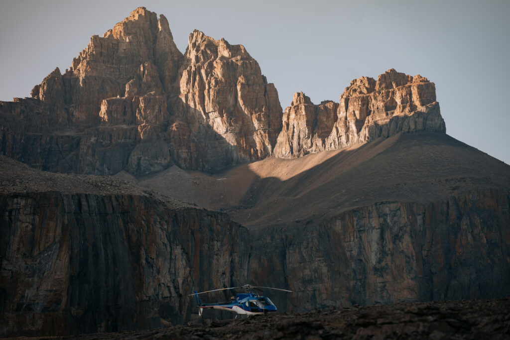 blue helicopter below mountain peaks lit up in alpenglow